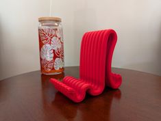 a red object sitting on top of a wooden table next to a glass jar filled with liquid