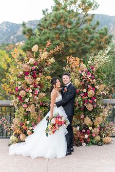 a bride and groom standing in front of an arch with colorful flowers on it at their wedding