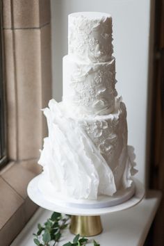 a three tiered white cake sitting on top of a table next to a window