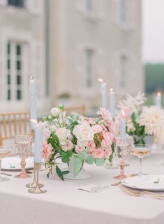 the table is set with white and pink flowers in vases, candles, and plates