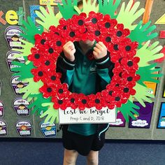 a young boy standing in front of a wreath made out of red and green paper flowers