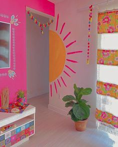 a living room with pink walls and colorful decorations on the wall, potted plant in front of window