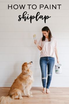 a woman is painting the wall with her dog and holding a paint roller in front of her