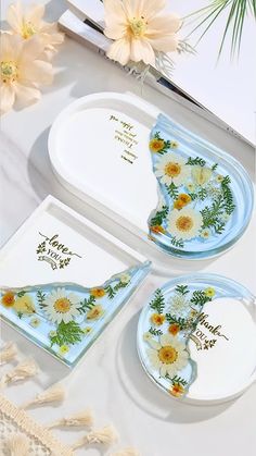 two plates with flower designs on them sitting next to each other and some flowers in the background