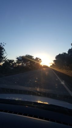 the sun is setting behind some trees on the side of the road as seen from inside a car