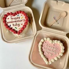 two heart shaped cakes in small containers with spoons on the side, one decorated like a happy anniversary baby