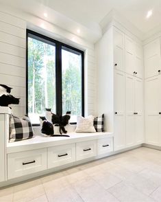 a white room with black and white pillows on the window sill, and two cats sitting on the windowsill