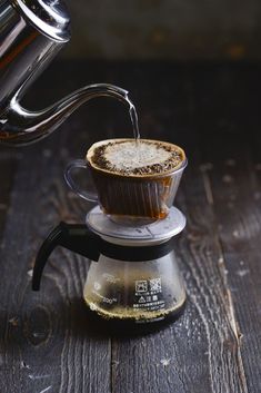 an espresso being poured into a glass cup on top of a wooden table