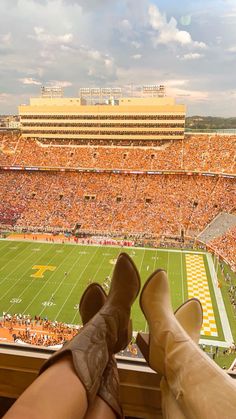 a person's feet and legs are on the edge of a football field as an orange stadium stands in the background