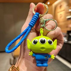 a hand holding a green and blue toy keychain