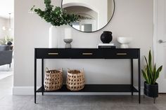 a black console table with two baskets and a round mirror on the wall above it