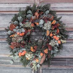 a wreath with orange flowers and greenery hanging on a wooden wall