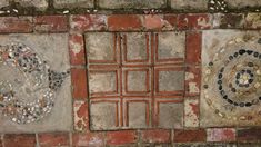 two decorative tiles on the side of a brick wall, one with a circular design