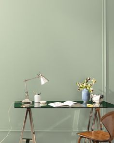 a desk with a chair and lamp on it in front of a green painted wall