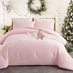 a bed with pink sheets and pillows in front of a white brick wall decorated for christmas