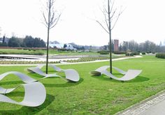 some white benches sitting in the grass near trees