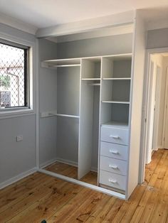 an empty room with white shelves and drawers in the corner, next to a window