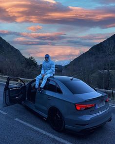 a man sitting on the open door of a car with mountains in the background at sunset