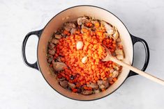 carrots and mushrooms are being cooked in a pot with a wooden spoon on the side