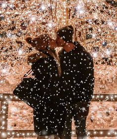 two people standing in front of a christmas tree with snow falling all around them and lights on the trees