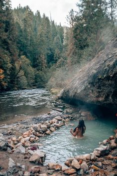 a woman is sitting in the middle of a river with steam coming out of it