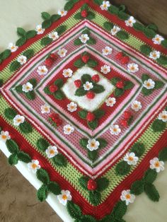 a crocheted square with flowers and leaves on it, sitting on a table