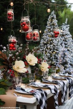 a table set for christmas with candles and ornaments hanging from the trees in front of it