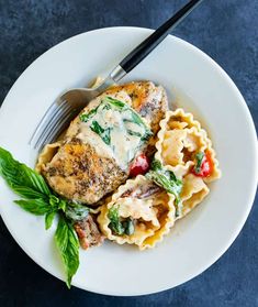 a white plate topped with pasta and meat covered in sauce, garnished with green leaves