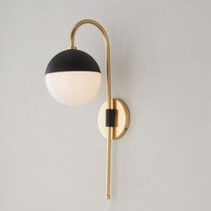 a black and gold wall light with a white ball hanging from it's side