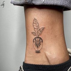 a woman's ankle with a small tattoo on the side of her leg and a plant in a vase