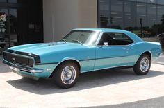 a blue muscle car parked in front of a building