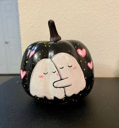 a black and white painted pumpkin with two hearts on it's face, sitting on a table