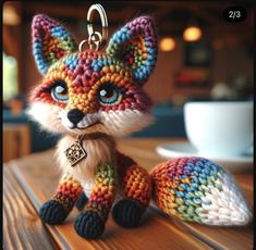 a knitted fox keychain sitting on top of a wooden table next to a cup