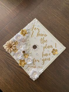 a white graduation cap with gold flowers on it sitting on top of a wooden table