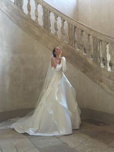 a woman in a white wedding dress standing next to a stair case and looking up at the sky