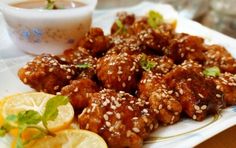 a white plate topped with meat covered in sesame seeds and garnished with lemon wedges