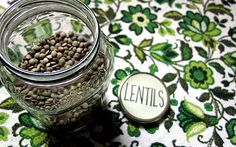 a glass jar filled with seeds sitting on top of a floral table cloth next to a button