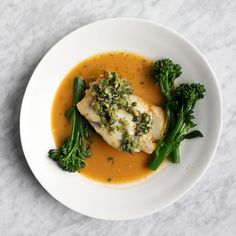 a white plate topped with meat and broccoli covered in gravy on top of a marble table