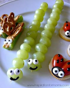 an assortment of food items on a white plate with grapes and pretzels in the shape of ladybugs