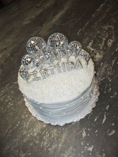 a white cake topped with lots of silver disco balls and the words happy birthday written on it