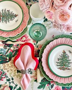 a table topped with plates covered in pink flowers and green trimmings next to white dishes