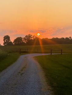 the sun is setting over an open field with a dirt road in front of it