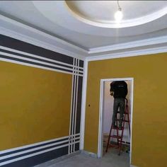 a man standing on a ladder in an empty room with yellow walls and black stripes