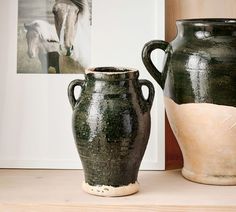 two black vases sitting next to each other on a wooden shelf in front of pictures