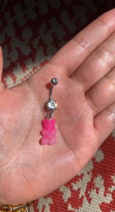 a person's hand holding a pink and silver belly ring with a teddy bear dangling from it