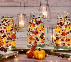 three glass jars with fall leaves on them and some candles in front of the jars