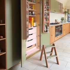 an open cabinet door in a kitchen next to a table and shelves on the wall