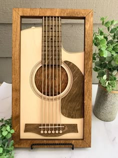 an acoustic guitar in a wooden frame next to potted plants