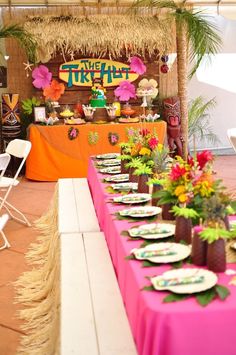 a table set up with plates and flowers for a tropical themed birthday party at the tiki hut