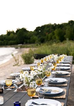 a long table is set with plates and silverware for an outdoor dinner by the water